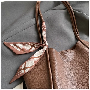 Dettaglio del manico della borsa tote marrone con trama litchi e foulard decorativo