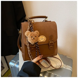 Detail of vintage brown backpack with cute plush bear charm and embroidery on luggage