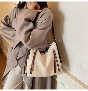 Macro detail of creamy hobo bag featuring dark brown tassels and soft faux leather texture