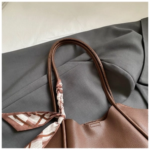 Dettaglio di una borsa tote grande in pelle marrone con foulard e manici arrotondati