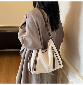 Detail view of a cream hobo bag with brown zipper accents shown in a lifestyle setting