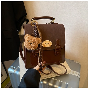 Close-up of retro brown backpack featuring stitching detail and bear plush pendant