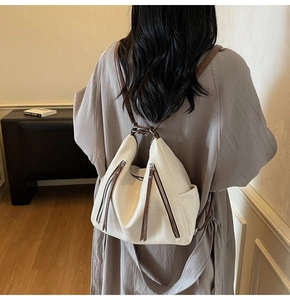 Back view of a woman wearing a minimalist cream high-capacity backpack with brown straps