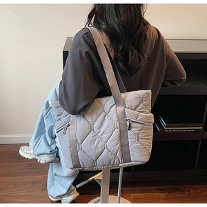 Grey quilted tote bag with side zipper and diamond pattern worn by a model