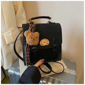 Detail of a vintage black mini backpack with a cute bear charm and tassel on a suitcase