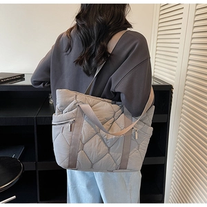 Detail of grey quilted tote bag featuring side metal zippers and wide fabric straps