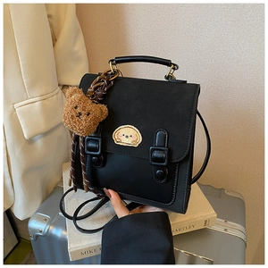 Detail of vintage black PU backpack with animal embroidery and plush bear charm on a suitcase