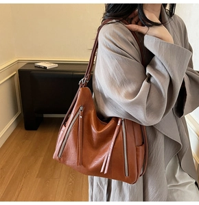 Detailed view of caramel brown tote bag featuring decorative zippers and long leather tassels
