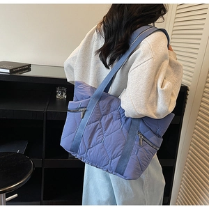 Blue quilted puffer tote bag shown on a model highlighting its large size and soft texture