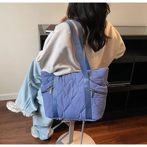 Detail view of the blue quilted tote bag featuring side silver zippers and wide strap
