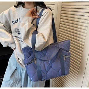 Blue quilted tote bag with metal zipper pocket shown on shoulder for daily commute use