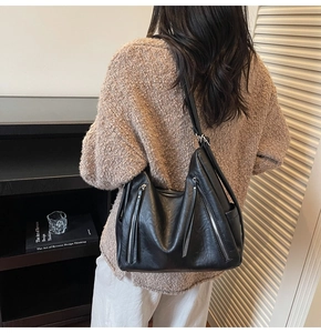 Close-up of black leather tote bag featuring vertical zipper detail and wide strap