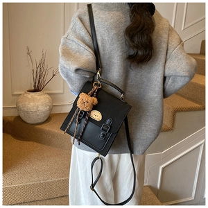 Detail of a black leather-style vintage backpack with a cute bear plush keychain