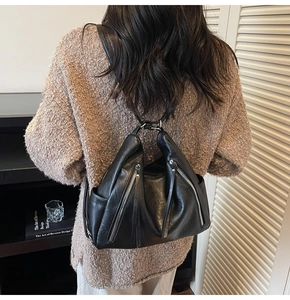 Detail of minimalist black leather backpack with metallic zippers and side pockets on model