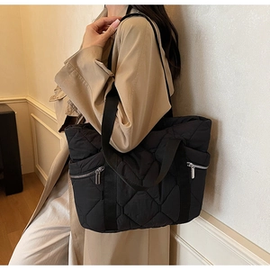 Detail of black quilted tote bag with silver zippers and high-density nylon texture