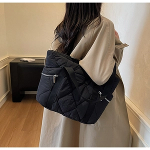 Detail of black quilted tote bag with silver zipper pocket shown on a model