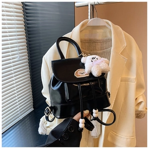 Detail of a black PU leather backpack featuring bread embroidery and a plush puppy charm