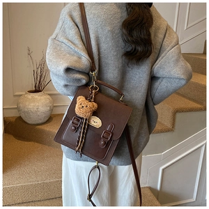 Detail of a dark brown vintage PU leather messenger bag with a cute plush bear pendant
