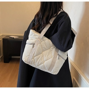 Detail of white quilted puffer tote bag with silver zippers and wide woven shoulder strap