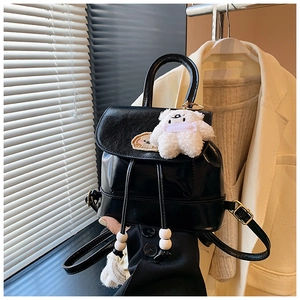 Detail of a black leather mini backpack with a drawstring closure and plush bear pendant