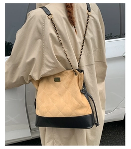 Close-up of quilted beige suede bucket bag with black leather base and gold chain