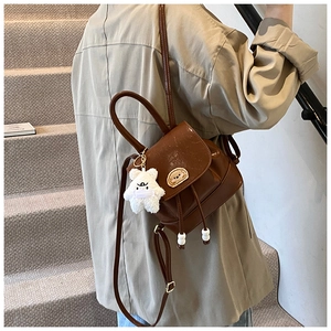 Close-up of vintage brown leather backpack with dog badge and white plush bear charm