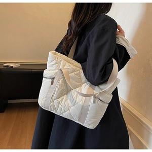 Close-up of white quilted tote bag with side zipper pocket and beige fabric shoulder strap