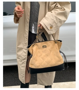 Quilted tote bag with leather patchwork and gold chain strap shown on a camel coat