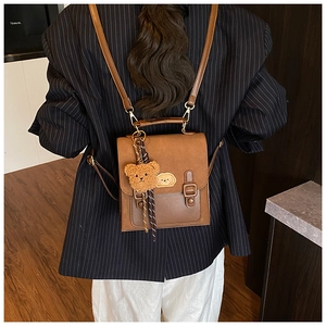 Detail of vintage brown leather backpack with bear charm on model's back