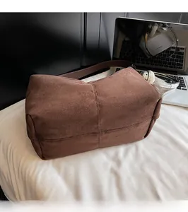Macro shot of deep brown suede tote bag with cross-stitch design on white bedding