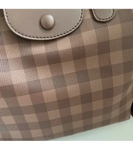 Detail of the brown plaid tote bag showing handle attachment and metal snap fastener