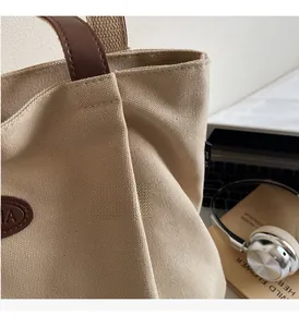 Close-up of pleated beige canvas tote with brown leather handle and brand logo details