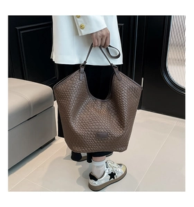 Detail of a large brown woven tote bag with Intrecciato craftsmanship and leather handles