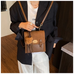 Detail of a brown vintage crossbody bag with a cute dog patch and plush bear pendant