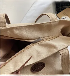 Detailed close-up of smooth metal zipper and brown leather brand tag on beige canvas tote bag