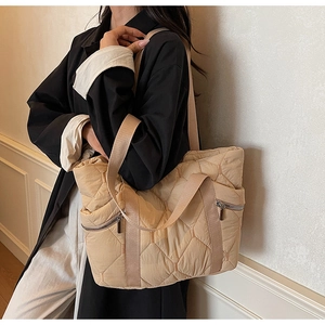 Detail of beige quilted tote bag with dual metal zippers and woven shoulder straps