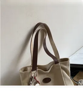 Detail of canvas tote bag with brown leather handles and a brand logo patch