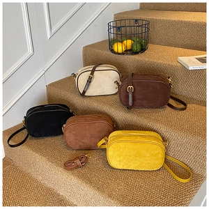 Five assorted matte crossbody camera bags displayed on steps in warm minimalist interior