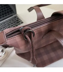 Close-up of a smooth metal zipper and braided puller on a brown checkered tote bag