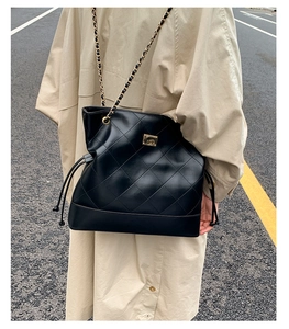 Detail of black quilted leather shoulder bag with gold chain strap on beige trench coat