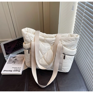 Close-up of white quilted puffer tote bag with side metal zippers and soft fabric handles