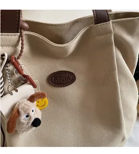 Detail of beige canvas tote with brown leather handles and cute plush puppy charm