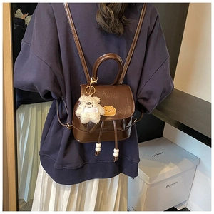Detail of dark brown leather backpack with drawstring closure and plush bear pendant