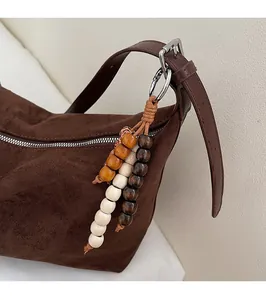 Détail d'un sac bandoulière en daim marron foncé avec pendentif en perles de bois tricolores