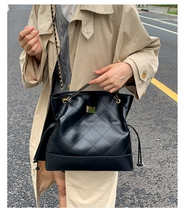 Close-up of quilted black leather hobo bag with gold hardware worn by a model in a trench coat