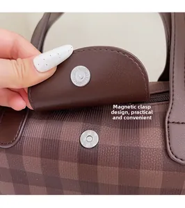 Close-up of magnetic snap closure on a brown checkered tote bag with leather trim