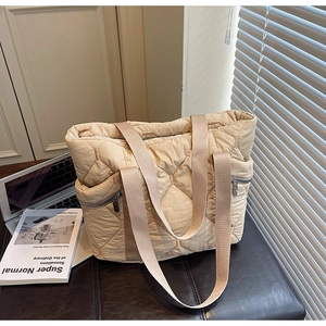 Close-up of beige quilted tote bag showing diamond stitching and silver side zipper pocket