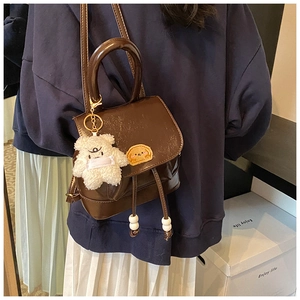 Deep brown faux leather backpack detail showing a plush bear charm and vintage handle