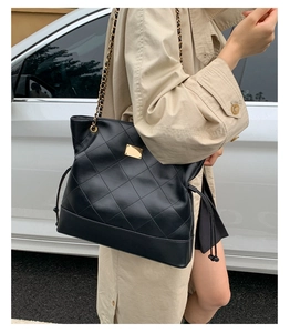 Detail of black quilted tote bag with gold chain strap and polished metal plate