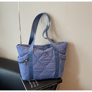 Close-up of blue quilted tote bag with side zipper pockets on a minimalist background